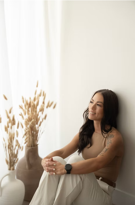 Stephanie George sitting by a sunlit window beside dried grasses, looking thoughtfully into the distance